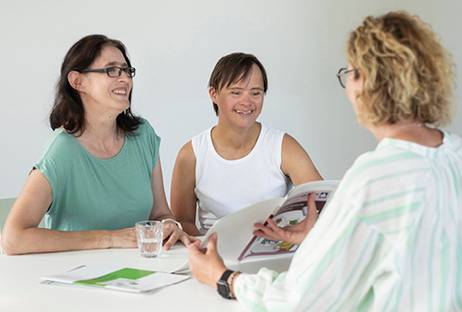 Drei Personen sitzen an einem Tisch und befinden sich in einem Beratungs-Gespräch. Drei Personen sitzen an einem Tisch und befinden sich in einem Beratungs-Gespräch.